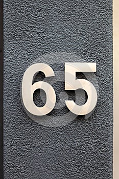 Number 65 metal house number on black wall