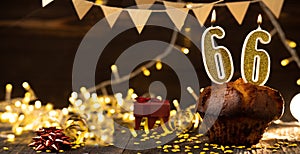 Number 66 golden festive burning candles in cake, wooden holiday background. sixty-six years of birth. the concept of