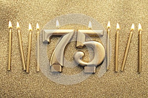 Number 75 gold celebration candle on a glitter background