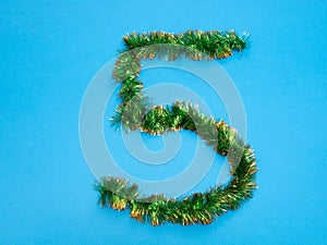 Number five 5 made of green tinsel on blue background