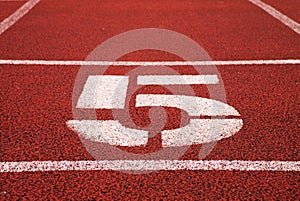 Number five. Big white track number on red rubber racetrack. Gentle textured running racetracks in stadium.