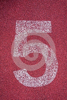 Number five on running track. White track number on red rubber racetrack
