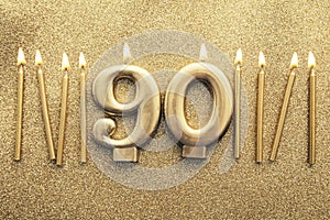 Number 90 gold celebration candle on a glitter background