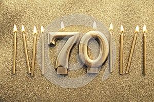 Number 70 gold celebration candle on a glitter background