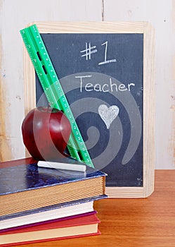 Number one teacher is written on a messy black chalkboard with old books in front. photo