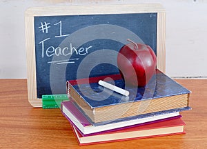 Number one teacher is written on a messy black chalkboard with old books in front. photo