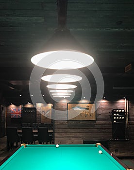 A number of pendant lamps illuminate a billiard table with green coating and billiard balls.