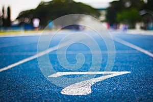 Number seven on the start of a running track .Blue treadmill with different numbers and white lines.Selective focus on Number.