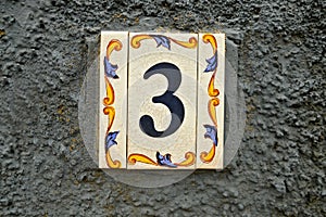 Number three, 3, on an elegant tile on a gray wall background.