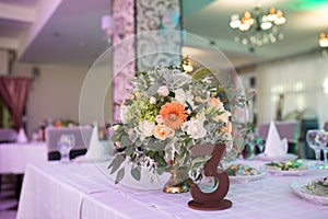 Number three and rustic flower arrangement with beige roses at table for guests on wedding hall. Wedding