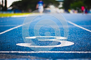 Number three on the start of a running track .Blue treadmill with different numbers and white lines.Selective focus on Number.