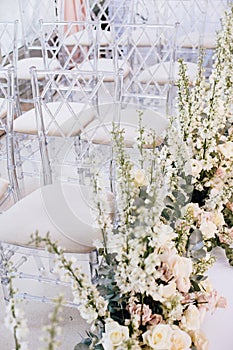 A number of transparent designer chairs at the wedding ceremony alongside beautiful floral arrangements of roses and buttercups