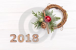The numbers 2018 and wreath of pine branch and cone on white wooden background