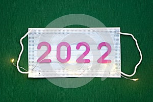 The numbers 2022 lie on a medical mask on a green background. Happy New Year, Christmas and Health concept