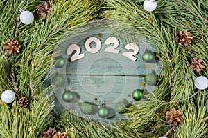 Numbers 2022 on a wooden background inside a circle of pine branches and balls. Beautiful new year or christmas card top view