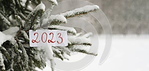 The numbers 2022 are written on paper with a snowy Christmas tree in the background. Snow is falling. Selective focus, blurred