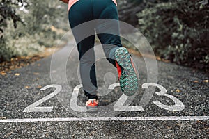 Numbers 2023 written on the asphalt road and female runners are starting to run ready for new year. New Year 2023 with