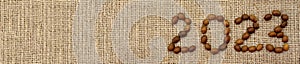 Numbers 2023 are made from coffee beans on fabric with burlap texture. Top View. Place for text. Background for design.