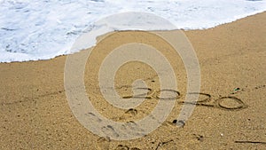 Numbers 2020 year on the sea shore, message handwritten in the golden sand on beautiful beach background