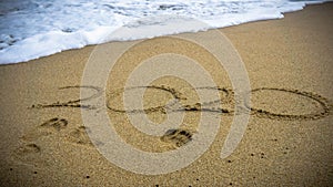 Numbers 2020 year on the sea shore, message handwritten in the golden sand on beautiful beach background
