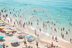 Numerous people of all ages packed on a beach on a sunny day, enjoying the sun, sand, and water, A crowded beach on a sunny day