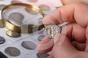 Numismatics. Old collectible coins made of silver on a wooden table. A collector holds an old coin.Ancient coin of the Roman photo