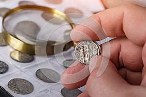 Numismatics. Old collectible coins made of silver on a wooden table. A collector holds an old coin.Ancient coin of the Roman