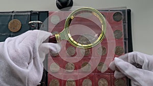 Numismatist examining old coin with magnifying glass closeup