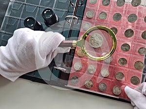 Numismatist in gloves examines collection of coins through magnifying glass
