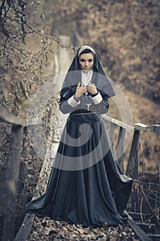 Nun stand on the wooden bridge with black cloak,cross,X.