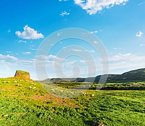 Nuraghe and herd of sheep on a green hill in Sardinia