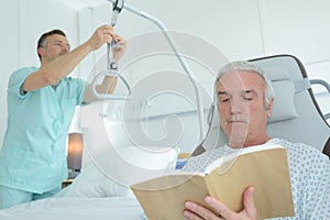 Nurse adjusting hoist patient reading book