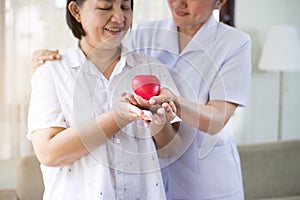 Nurse and Asian elderly woman holding heart red model on hands together,Senior healthy and taking care concept