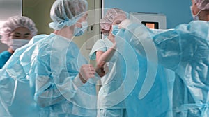 Nurse and assistant dressing surgeon gown in surgery room