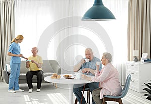 Nurse assisting elderly man while senior couple having breakfast