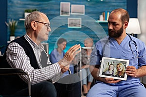 Nurse assisting elderly man with video call in nursing home