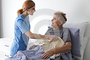 Nurse assisting elderly woman in bed