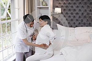 Nurse assisting female patient suffering with back pain on bed
