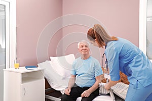 Nurse assisting senior man on bed