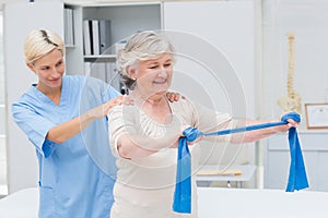 Nurse assisting senior patient in exercising with resistance band