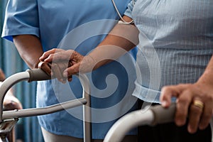 Nurse assisting senior patient in walking with walker at nursing home