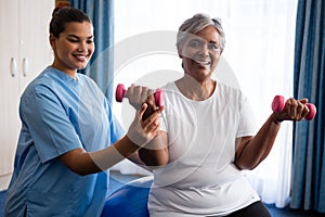 Nurse assisting senior woman in lifting dumbbells