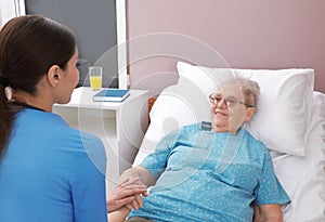 Nurse assisting senior woman lying on bed