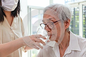 Nurse or caregiver gives water to senior woman,taking care,feeding water,thirsty asian old elderly drinking fresh water to quench