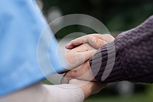 Nurse or caregiver hold hand of elderly patients to support and soothe walk by using walker in garden