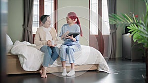 Nurse caregiver wearing scrubs exercises with a senior Asian woman to relieve a frozen shoulder of the senior patient.