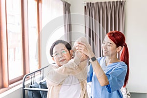 Nurse caregiver wearing scrubs exercises with a senior Asian woman to relieve a frozen shoulder of the senior patient
