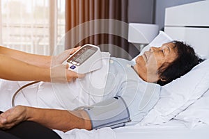 Nurse checking blood pressure of a senior woman on bed