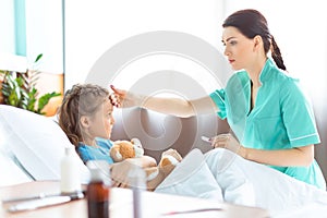 Nurse checking temperature of sick little girl in hospital bed