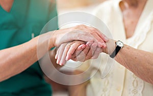 Nurse consoling her elderly patient by holding her hands